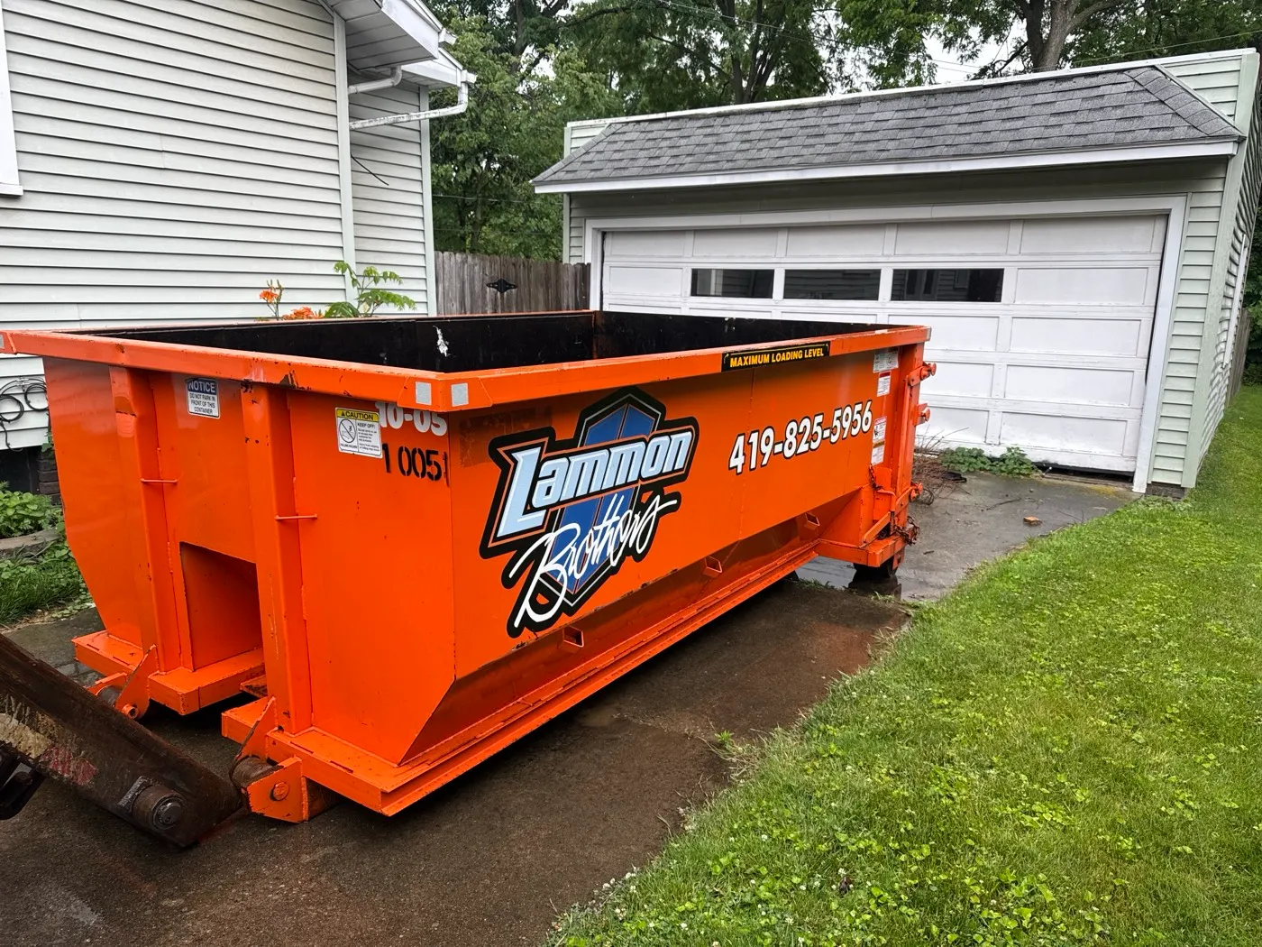 An empty Lammon Brothers roll-off dumpster on a driveway, open top and four-foot walls