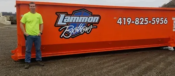 Owner standing beside a 40-yard Lammon Brothers roll-off dumpster for scale