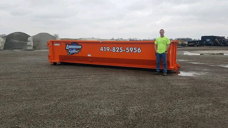 Orange 20-yard dumpster located in a yard setting in Toledo, Ohio, for rent. A man stands beside it to illustrate its substantial size and storage capacity. This dumpster is perfect for larger construction projects, major home renovations, or significant yard clean-ups.